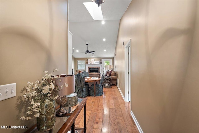 corridor with lofted ceiling with skylight and light wood-type flooring