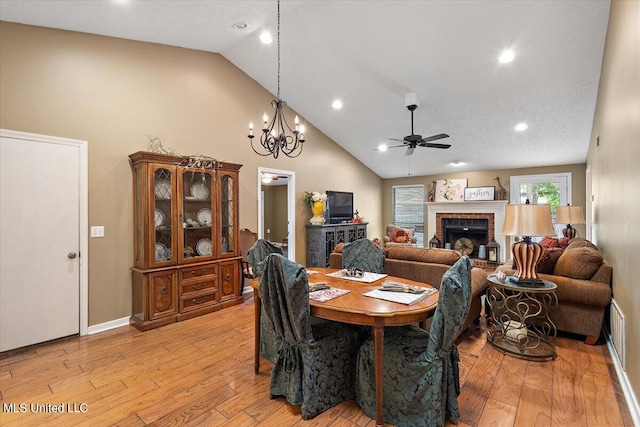 dining area featuring light hardwood / wood-style floors, high vaulted ceiling, ceiling fan with notable chandelier, and a fireplace