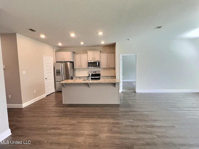 kitchen featuring an island with sink, stainless steel appliances, baseboards, visible vents, and dark wood-style floors