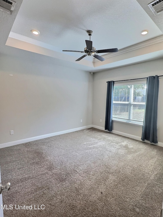 spare room with carpet floors, visible vents, baseboards, ceiling fan, and a raised ceiling