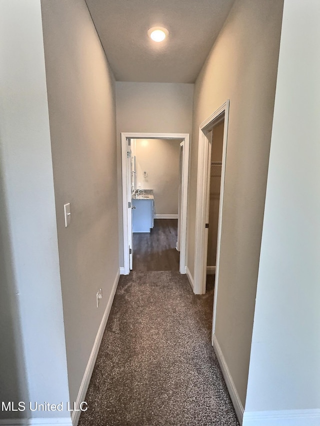 corridor with baseboards and dark carpet