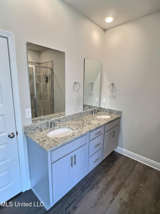full bathroom featuring double vanity, a shower stall, a sink, and wood finished floors