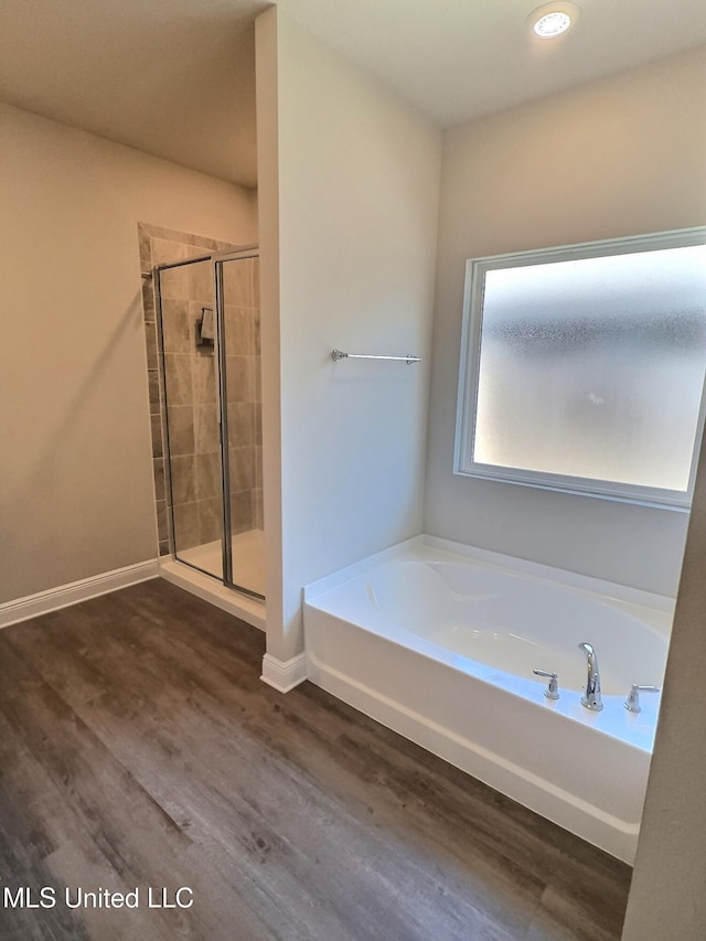 bathroom with wood finished floors, a stall shower, baseboards, and a bath