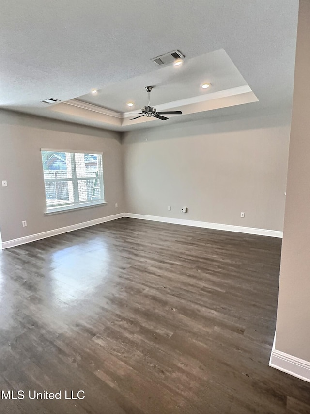unfurnished room with a ceiling fan, visible vents, dark wood finished floors, and a raised ceiling