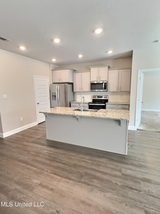 kitchen with visible vents, a kitchen island with sink, baseboards, a sink, and appliances with stainless steel finishes