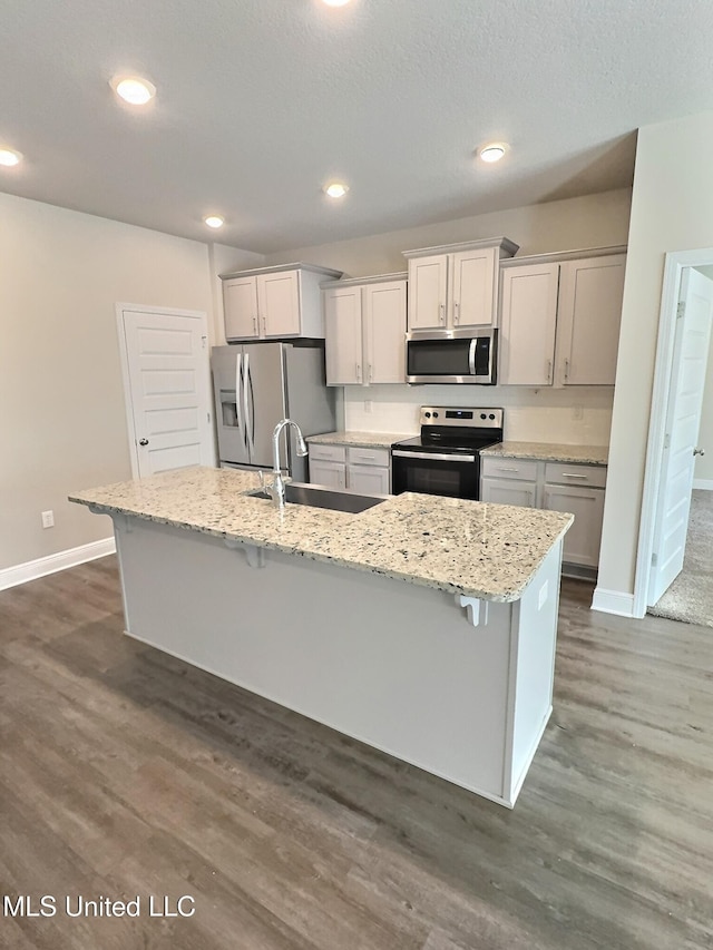 kitchen with a kitchen island with sink, a breakfast bar, baseboards, a sink, and appliances with stainless steel finishes