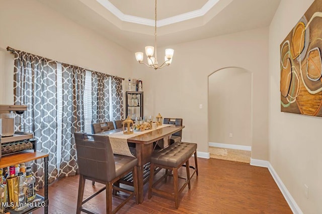 dining area with arched walkways, wood finished floors, baseboards, a raised ceiling, and an inviting chandelier