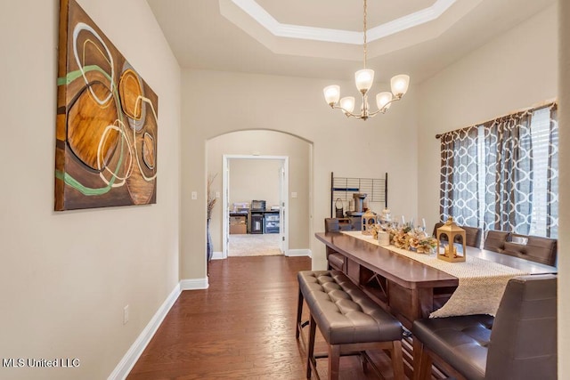 dining space featuring dark wood-style flooring, a notable chandelier, a raised ceiling, arched walkways, and baseboards