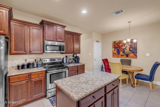 kitchen with light tile patterned flooring, light stone countertops, stainless steel appliances, decorative light fixtures, and visible vents