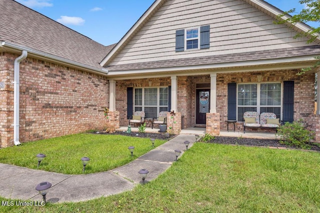 view of front facade featuring a porch, a front lawn, roof with shingles, and brick siding