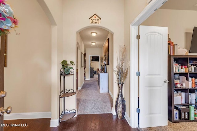 corridor featuring arched walkways, baseboards, and dark wood-style flooring