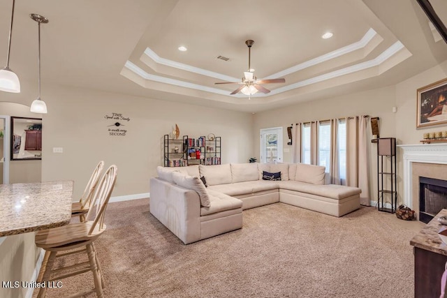 living area with ceiling fan, crown molding, a raised ceiling, carpet, and a premium fireplace