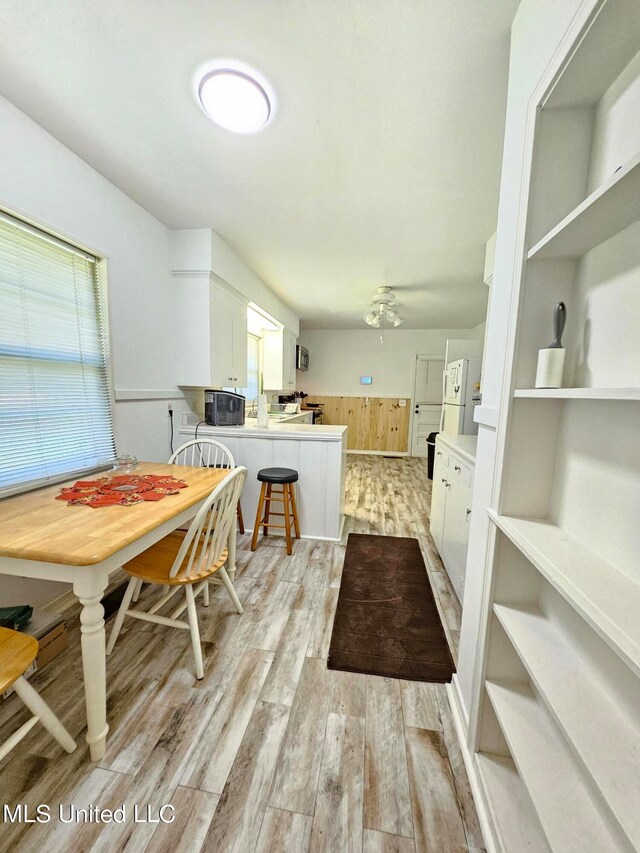 kitchen featuring light wood-type flooring, kitchen peninsula, white cabinetry, ceiling fan, and a breakfast bar area