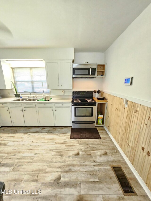 kitchen featuring wood walls, sink, white cabinetry, stainless steel appliances, and light hardwood / wood-style flooring