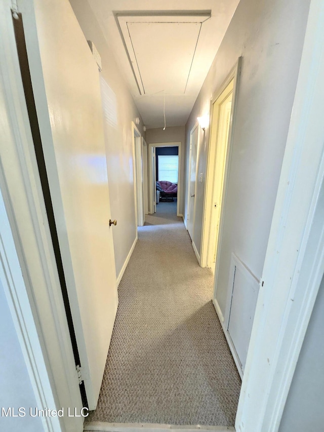 hall with baseboards, light colored carpet, and attic access