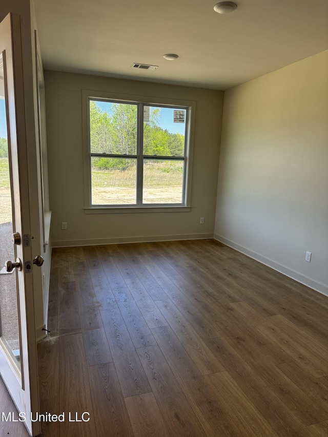 spare room featuring dark wood-style flooring, visible vents, and baseboards