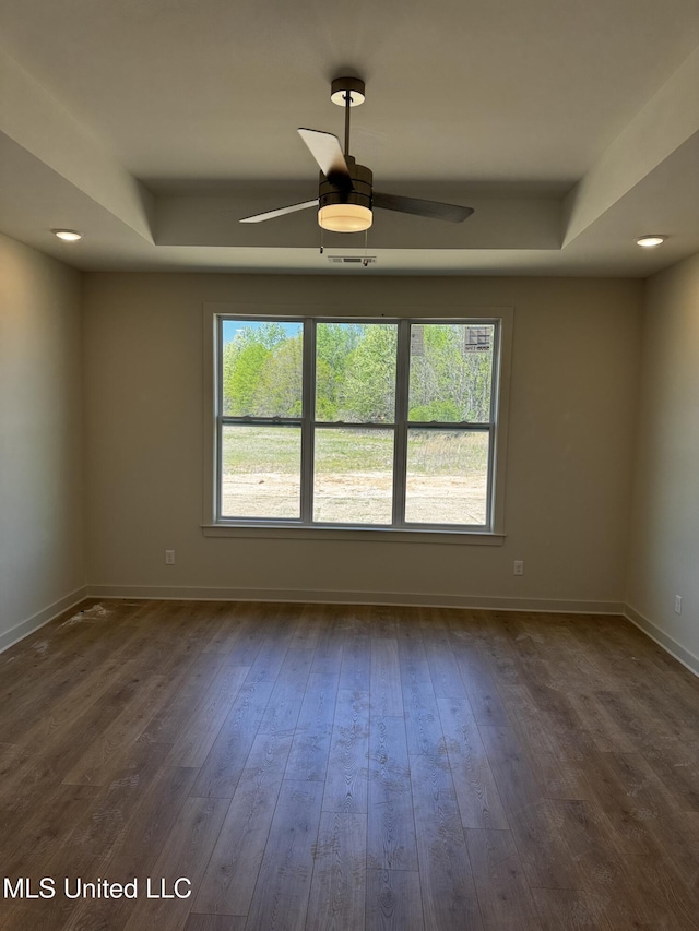 unfurnished room with a tray ceiling, dark wood-style flooring, baseboards, and a ceiling fan