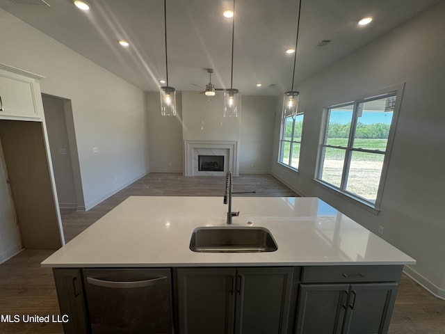 kitchen with a ceiling fan, wood finished floors, a kitchen island with sink, a sink, and a premium fireplace