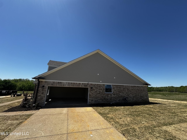 view of side of property with an attached garage, a lawn, driveway, and brick siding