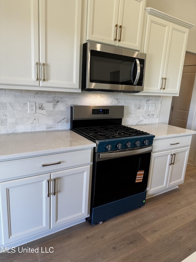 kitchen featuring range with gas cooktop, stainless steel microwave, white cabinetry, wood finished floors, and decorative backsplash