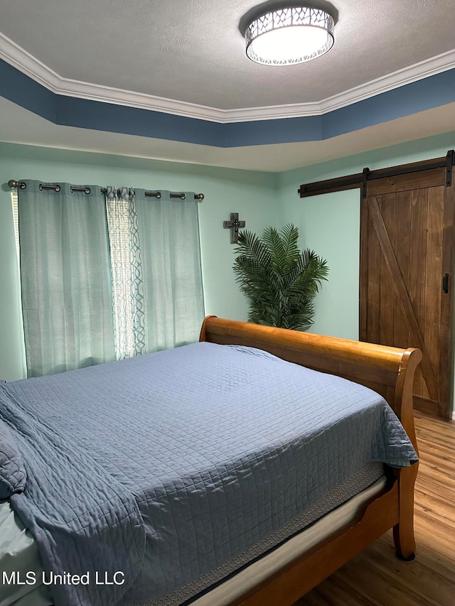 bedroom featuring ornamental molding, a textured ceiling, a barn door, and wood-type flooring