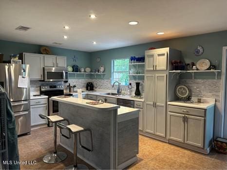 kitchen featuring sink, a center island, stainless steel appliances, gray cabinets, and a breakfast bar