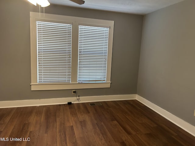 unfurnished room featuring dark wood-style floors, visible vents, baseboards, and a ceiling fan