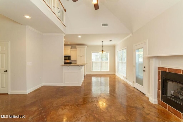 unfurnished living room with ceiling fan with notable chandelier, a fireplace, high vaulted ceiling, and crown molding