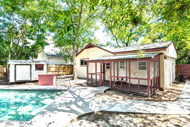 rear view of property featuring a patio, a swimming pool side deck, and a storage shed