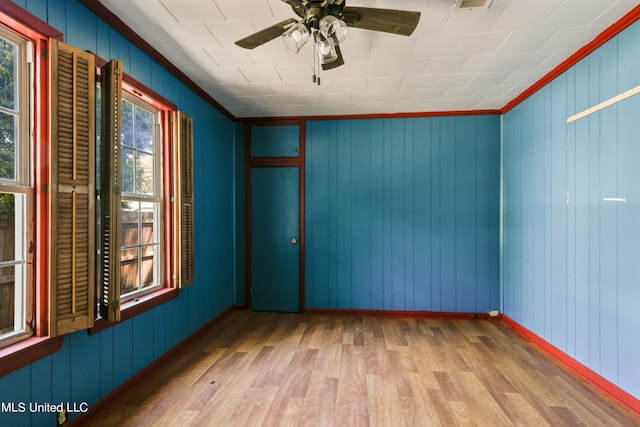 spare room with ceiling fan, crown molding, wooden walls, and hardwood / wood-style floors