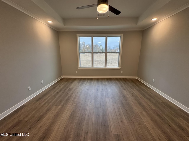 spare room featuring a raised ceiling, dark wood-type flooring, ornamental molding, baseboards, and ceiling fan