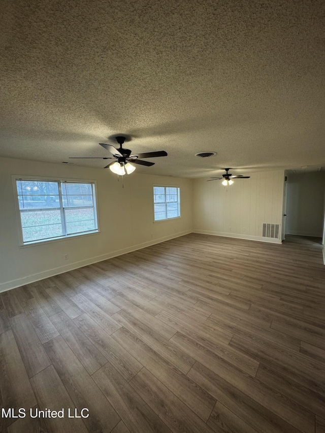 empty room featuring a textured ceiling, hardwood / wood-style flooring, a wealth of natural light, and ceiling fan