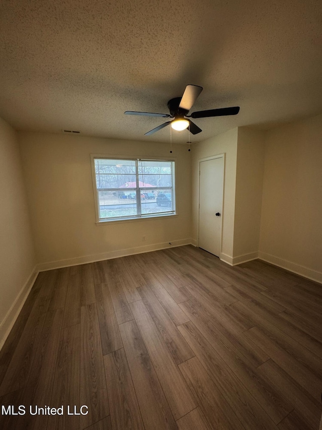 empty room featuring a textured ceiling, ceiling fan, and dark wood-type flooring