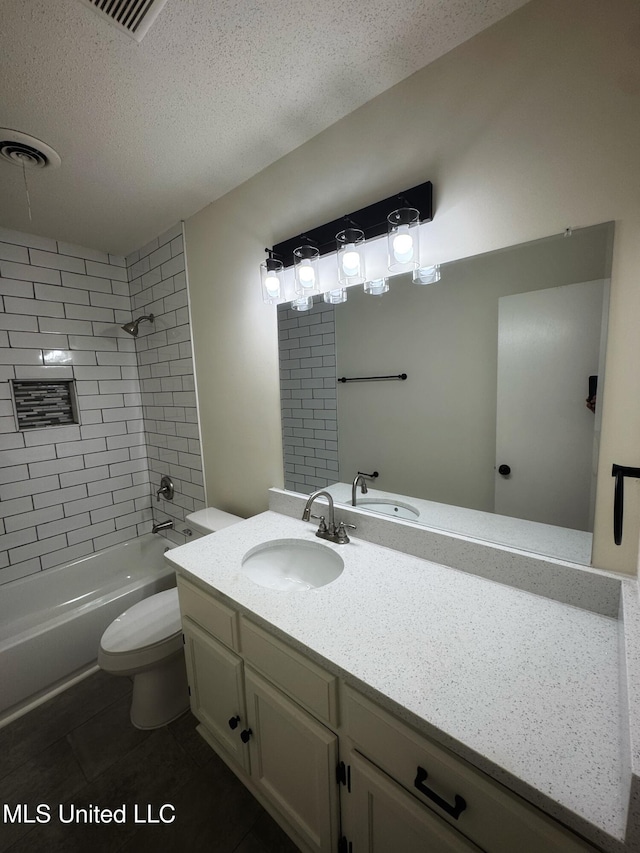 full bathroom featuring vanity, tile patterned floors, tiled shower / bath, toilet, and a textured ceiling