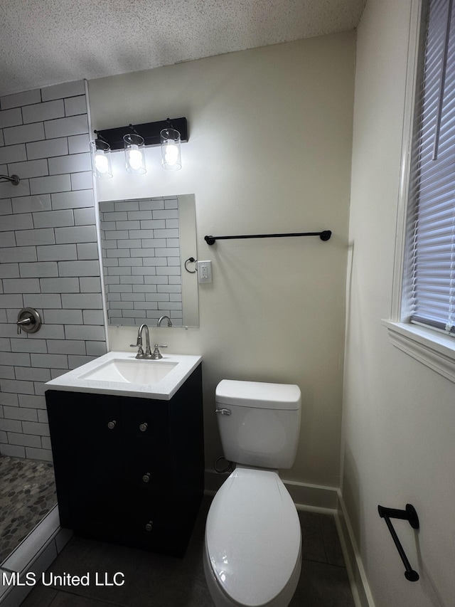 bathroom featuring vanity, tile patterned flooring, toilet, tiled shower, and a textured ceiling