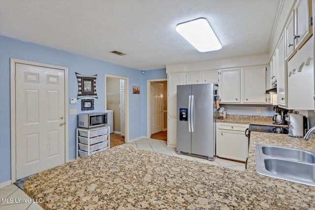 kitchen with a textured ceiling, appliances with stainless steel finishes, white cabinetry, sink, and light tile patterned flooring