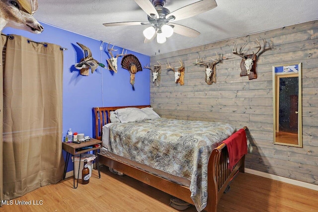 bedroom featuring a textured ceiling, hardwood / wood-style flooring, wooden walls, and ceiling fan