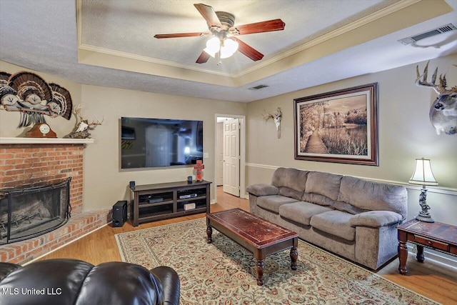 living room featuring a brick fireplace, a raised ceiling, ornamental molding, and a textured ceiling