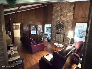 living room featuring vaulted ceiling with beams, wood walls, a stone fireplace, and wood-type flooring