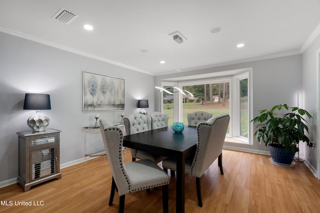 dining space with ornamental molding and light hardwood / wood-style flooring