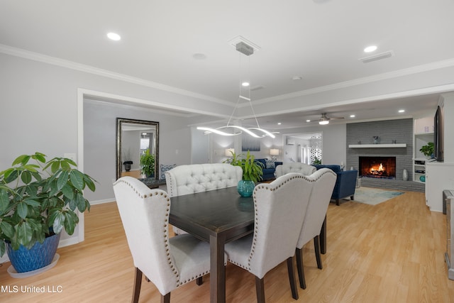 dining area featuring ornamental molding, a fireplace, light hardwood / wood-style floors, and ceiling fan