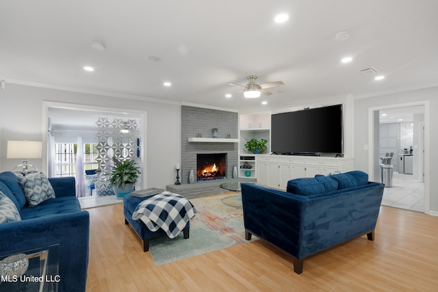 living room featuring light hardwood / wood-style floors, crown molding, a fireplace, and ceiling fan