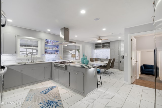 kitchen featuring tasteful backsplash, sink, island exhaust hood, stainless steel gas stovetop, and a breakfast bar