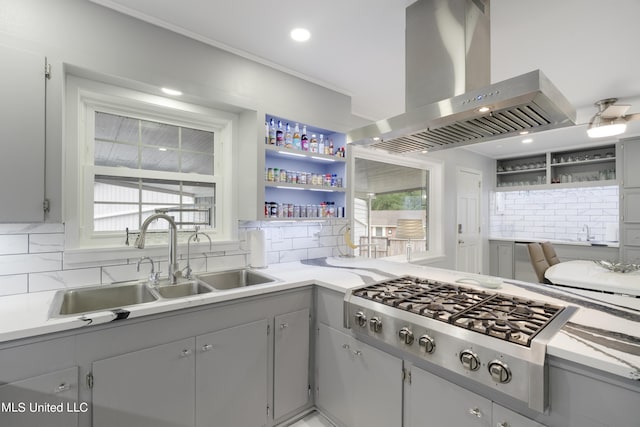 kitchen with gray cabinetry, sink, island range hood, backsplash, and stainless steel gas stovetop