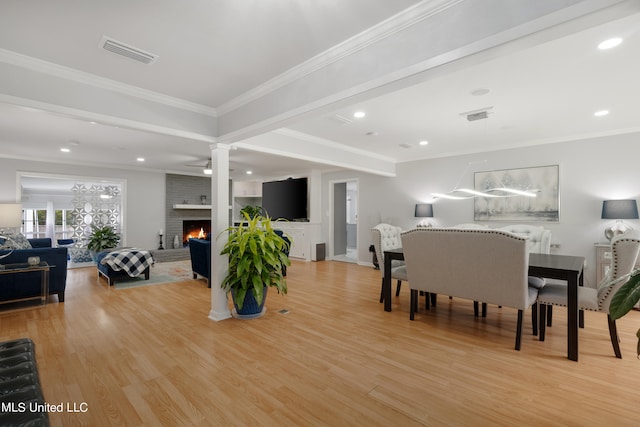 dining space featuring crown molding, light hardwood / wood-style flooring, a brick fireplace, and ornate columns