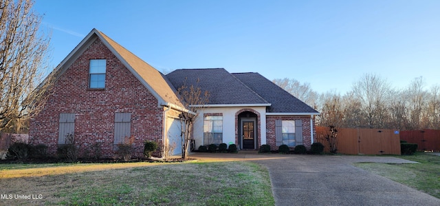 traditional-style house featuring an attached garage, brick siding, a shingled roof, a gate, and a front yard