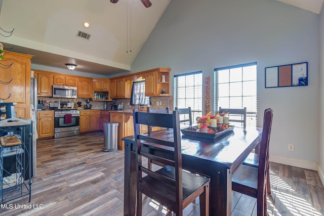 dining room featuring hardwood / wood-style floors, high vaulted ceiling, and ceiling fan