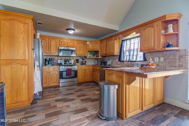 kitchen with kitchen peninsula, tasteful backsplash, a breakfast bar area, appliances with stainless steel finishes, and dark wood-type flooring