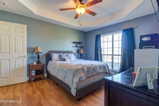 bedroom with ceiling fan, a raised ceiling, and hardwood / wood-style floors