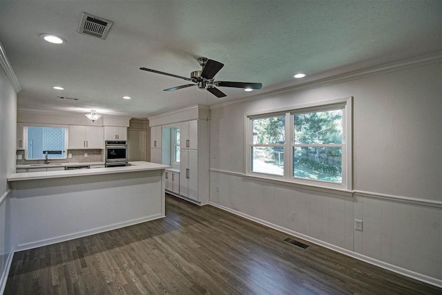 kitchen with kitchen peninsula, white cabinets, tasteful backsplash, and dark wood-type flooring